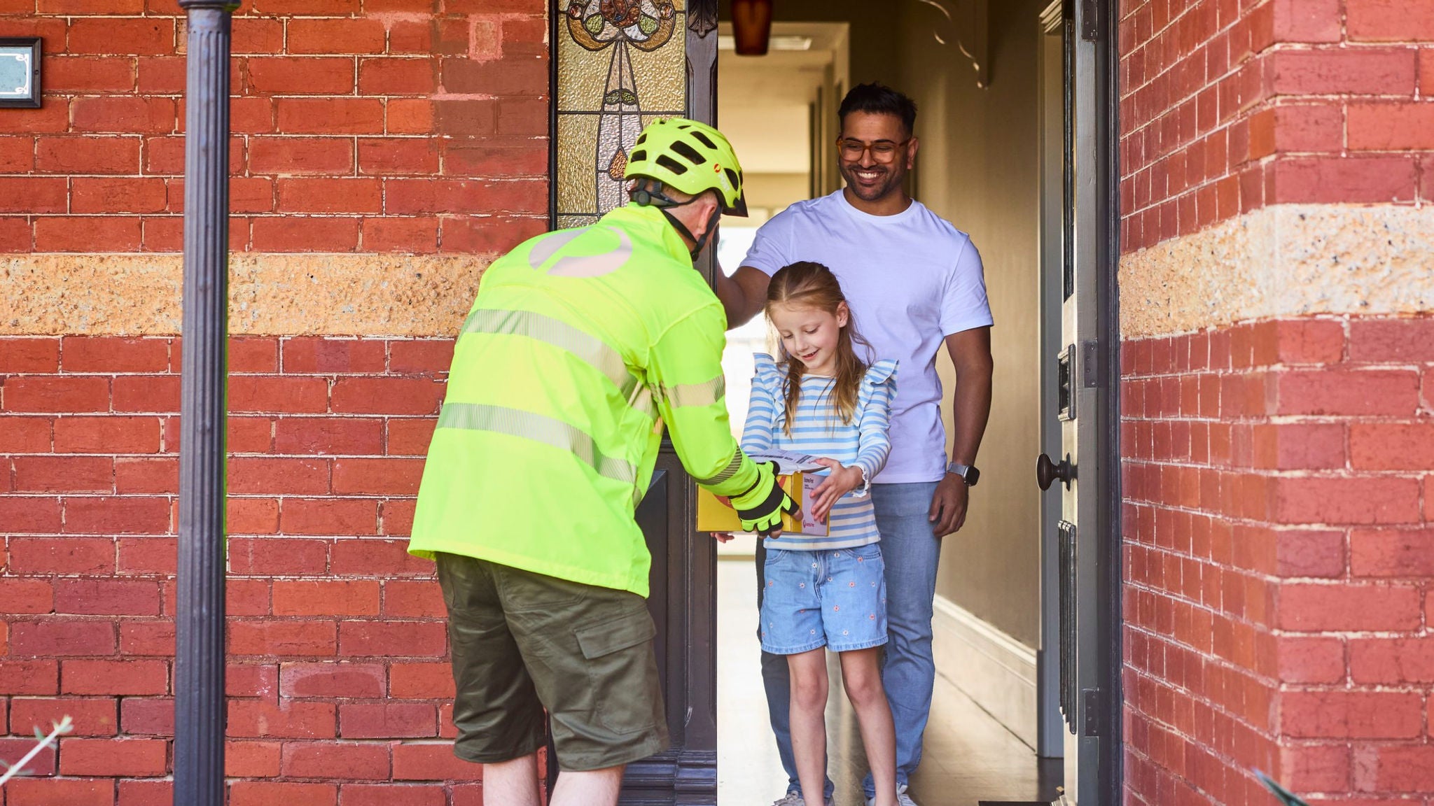 Delivery worker hands parcel to a young girl standing at a front door