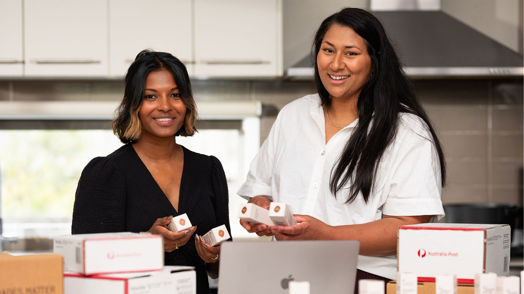 photo-two-young-olive-skinned-women-holding-boxes-of-foundation-and-standing-in-front-of-a-counter-strewn-with-cosmetic-products