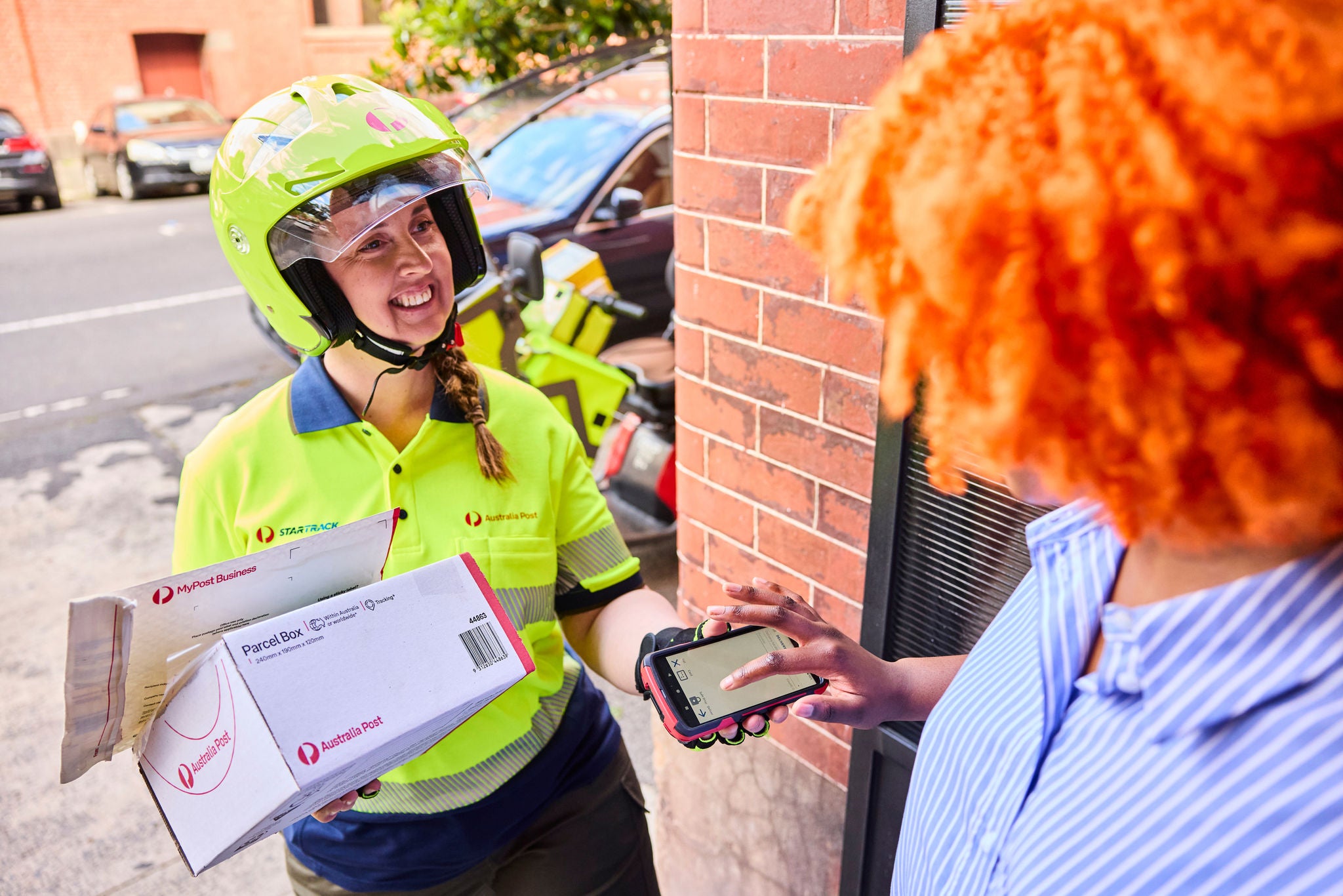 Woman signing for a parcel, being delivered by an Australia Post postie.